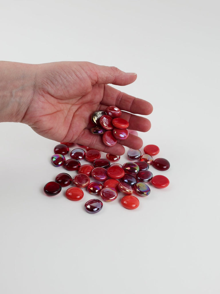 Video of red mix glass nuggets in bright red, cherry and burgundy shades with an iridescent sheen, 16–20 mm, picked up from a pile by hand and dropped back to show their size, round shape and shine